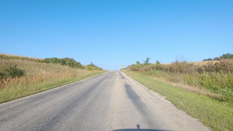 POV-driving-on-rural-county-road-with-no-center-line-past-fields,-pastures-and-farmyards-in-rural-Iowa-on-a-sunny-early-autumn-day---near-Kalona,-Iowa,-USA