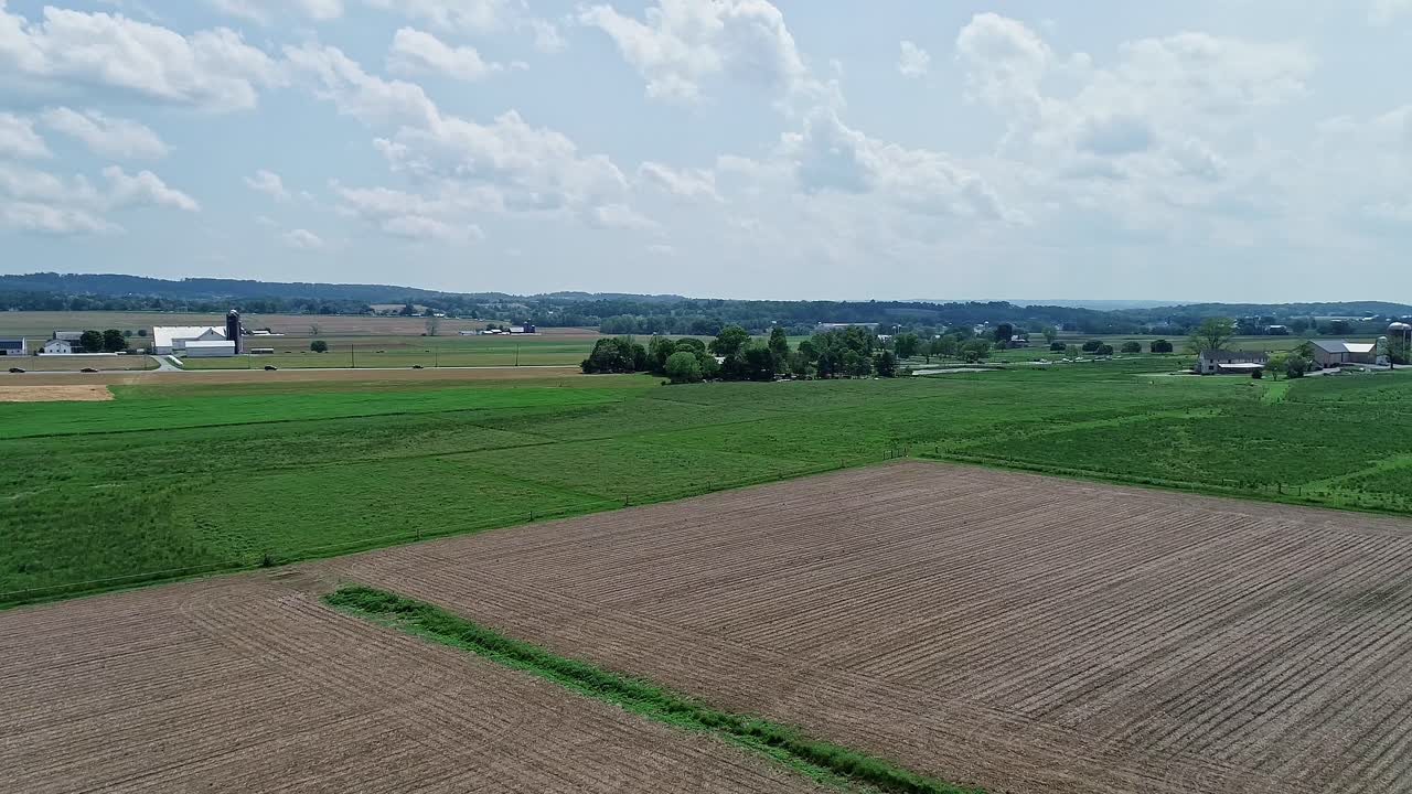 Eine langsame Luftaufnahme von Ackerland mit grünen und gepflügten Feldern an einem teils sonnigen Tag.