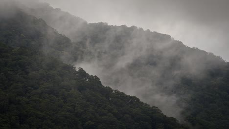 Misty-mountains-above-a-beautiful-majestic-valley-with-clouds-forming,-close-up-shot