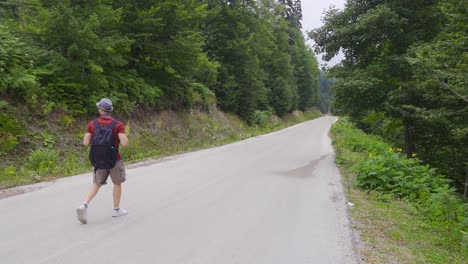 man in hat with backpack walking on empty road.