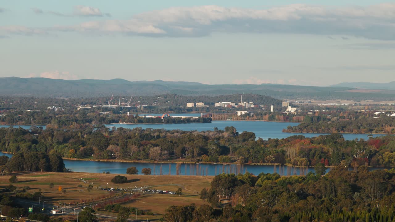 Distant view along Lake Burley Griffin towards the CBD with notable Canberra landmarks visible, framed by autumn colours and light.
