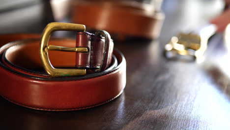 close up shot of a leather workshop and workbench with a brand new leather belt shining with a brass buckle as he works in slow motion