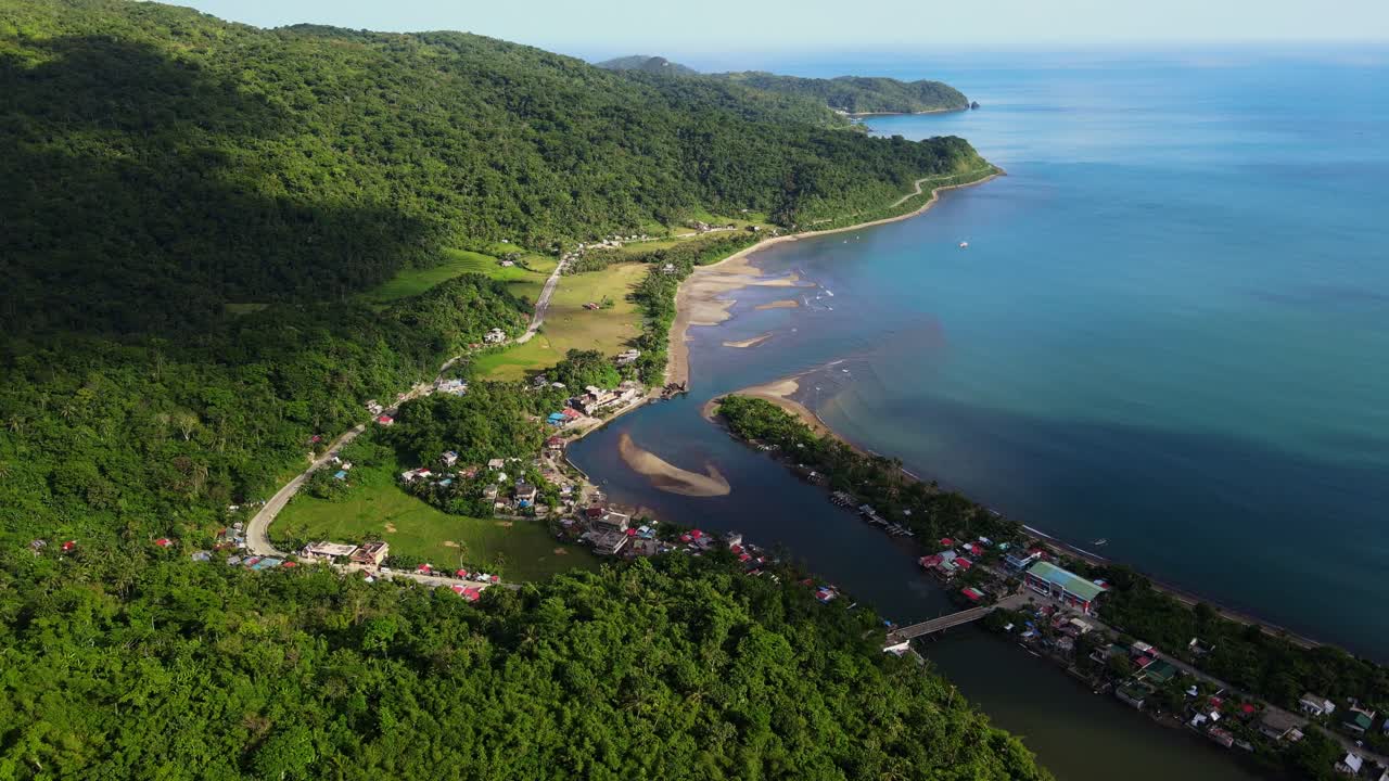 Panoramic aerial drone shot of coastal barangay town village Batalay with scenic lagoon and lush hills at tropical island Catanduanes, Philippines.