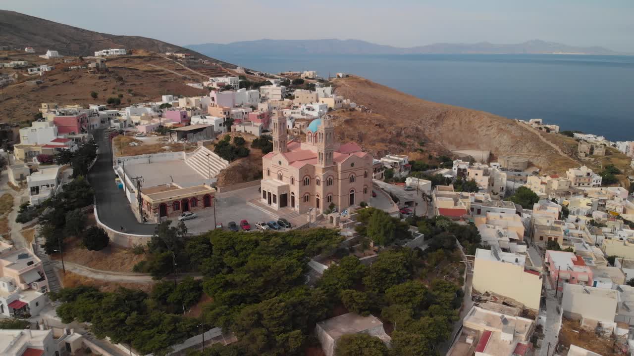 vuelo aéreo hacia atrás desde la hermosa iglesia en la cima de la colina en syros, grecia con el océano y otras islas en el fondo
