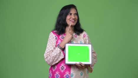 mature happy beautiful indian woman thinking while showing digital tablet