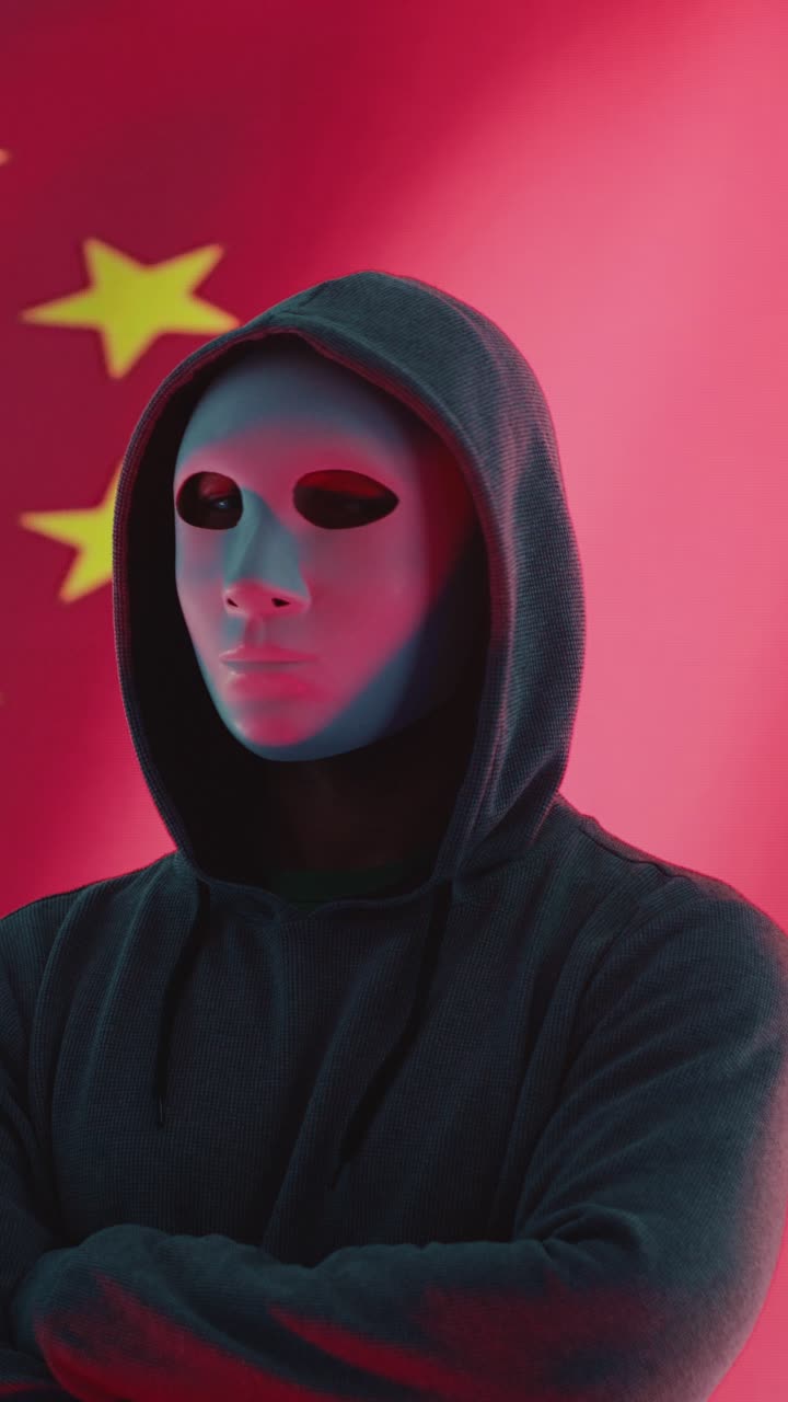 Hacker anonimo con maschera e felpa con cappuccio di fronte alla bandiera cinese