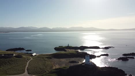 aerial view orbiting idyllic ynys llanddwyn island with hazy snowdonia mountain range across shimmering irish sea at sunrise
