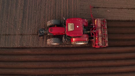 top view of a red tractor seeding corn on agriculture field. start of the planting season,