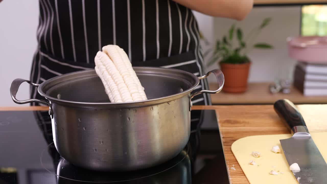 Un cuoco versa acqua bollente girando una pannocchia bianca con le pinze.