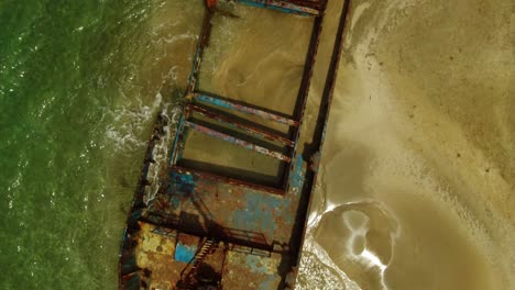 small waves wash across a rusted abandoned shipwreck on a golden sand beach, manzanillo, aerial top down