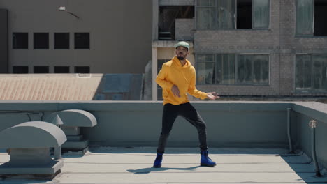 dancing man hip hop dancer performing freestyle dance moves on rooftop in city wearing yellow hoodie