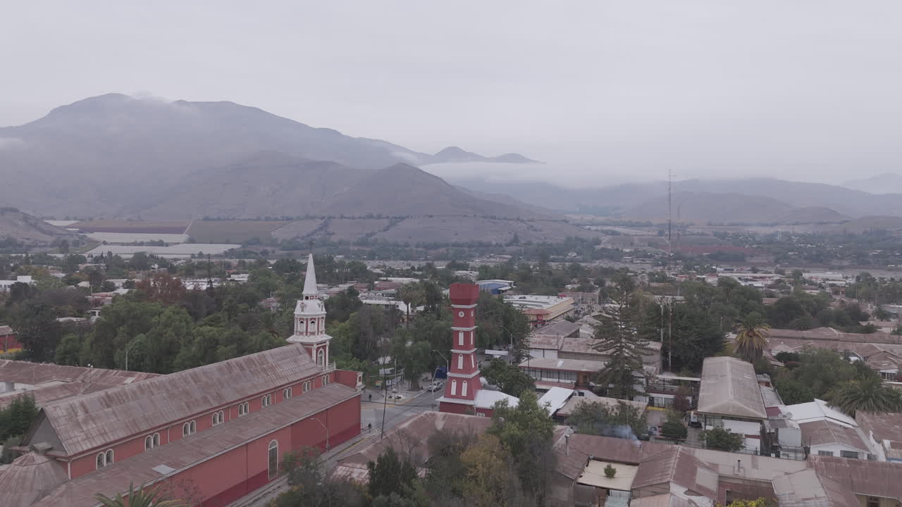 Upwards drone shot around the town of Vicuña near Coquimbo in Chile South America with the main square and red tower Torre Bauer visible on a grey day with mountains in the background LOG