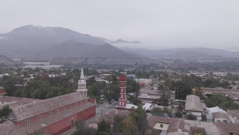upwards drone shot around the town of vicuña near coquimbo in chile south america with the main square and red tower torre bauer visible on a grey day with mountains in the background log