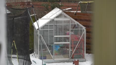 small glass greenhouse in garden during snowfall. slow-motion