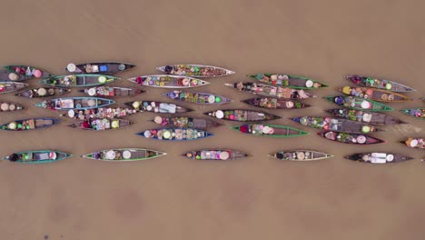 Colorful-boats-on-brown-river-getting-pulled-by-motorboat,-floating-market,-top-down