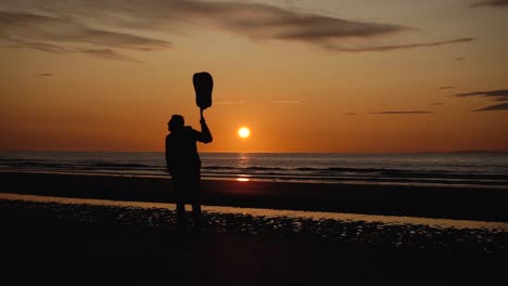 Man-running-with-guitar-in-back-sand-beach-at-sunset