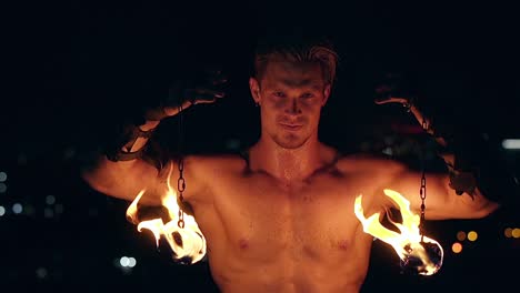 young blond male holds two pois hanging on chains male stares at camera slow motion shot close-up shot