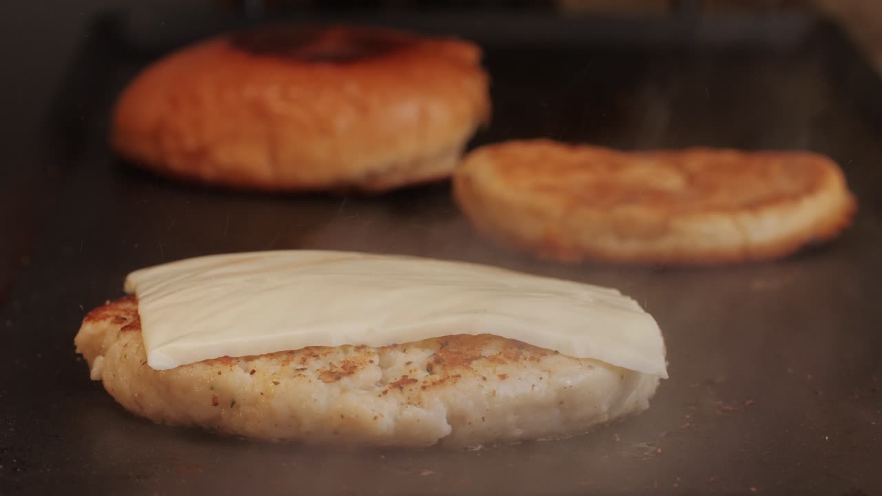 Cooking American fat smash burger on grill close-up. Chiken or fish cutlet smashing by burger press. The chef in kitchen of the restaurant making cutlets for burgers - smash burger beefsteak. Fast and street food concept. High quality 4k footage