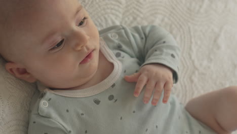 cute baby laying in white bed sheets, looking with curiosity, portrait in bright bedroom