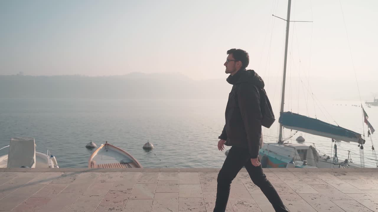 Man walking through city Salo italy, small town on lake garda. Following the promenade exploring the beautiful nature seascape and city with marina and sailboats in the background
