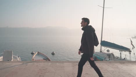 man walking through city salo italy, small town on lake garda. following the promenade exploring the beautiful nature seascape and city with marina and sailboats in the background