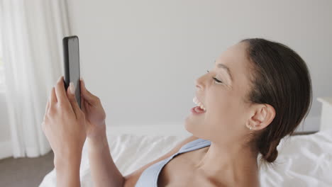 happy biracial woman lying on bed using smartphone, slow motion