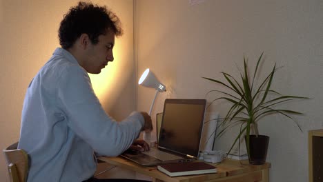 un hombre que trabaja en su computadora portátil en la oficina de su casa estornuda en su brazo para evitar la propagación del coronavirus - tiro cerrado