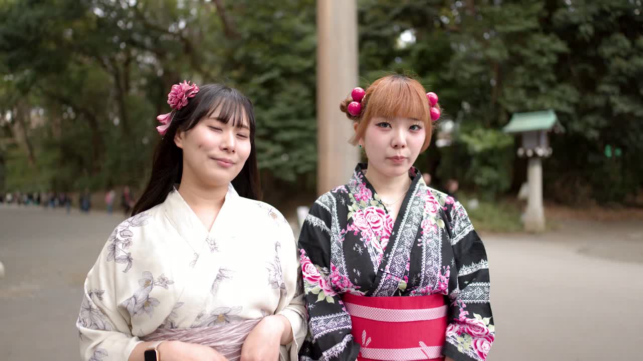 Two women wearing floral kimonos stand together outdoors at a traditional Japanese shrine in Tokyo