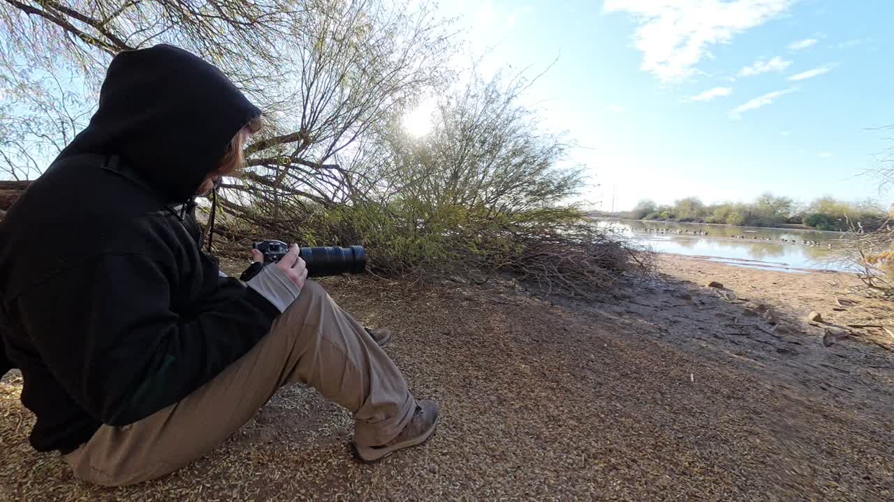 Red head man in black birding with a digital camera.