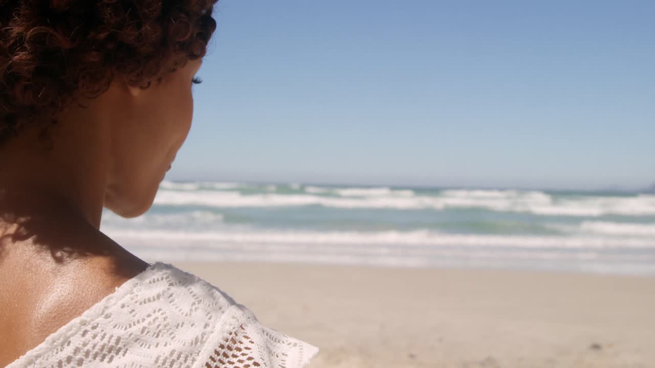 Vista posteriore di giovane donna afroamericana che si rilassa in spiaggia sotto il sole 4k