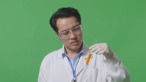 close up of unsatisfied asian man scientist looking at the orange liquid in the test tube and shaking his head being tired while standing on the green screen background in the laboratory