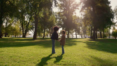 Daughter-holding-mom-hands-observing-park-field-in-golden-sunlight-together.
