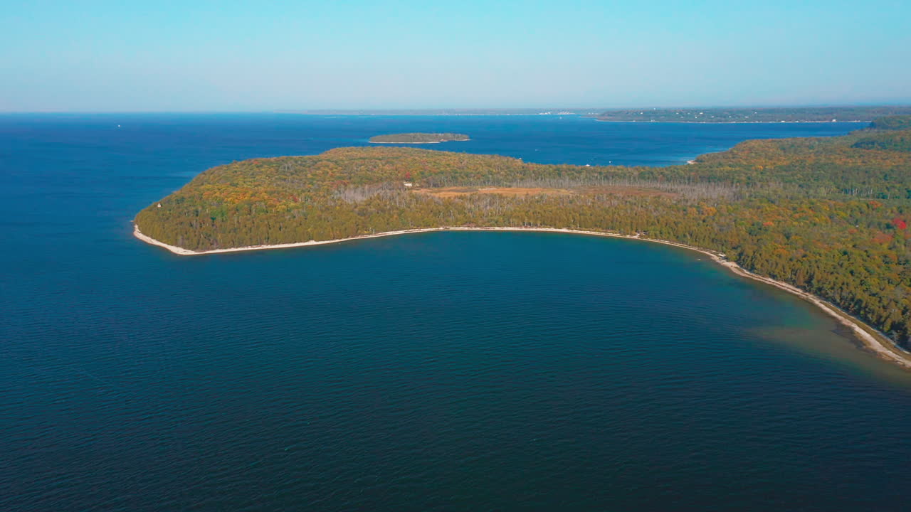 The Door County peninsula stretches into Lake Michigan beneath clear skies, its forested shoreline glowing with early autumn tones above calm blue water