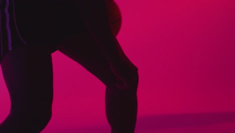 close up studio portrait of male basketball player dribbling and bouncing ball against pink lit background 5