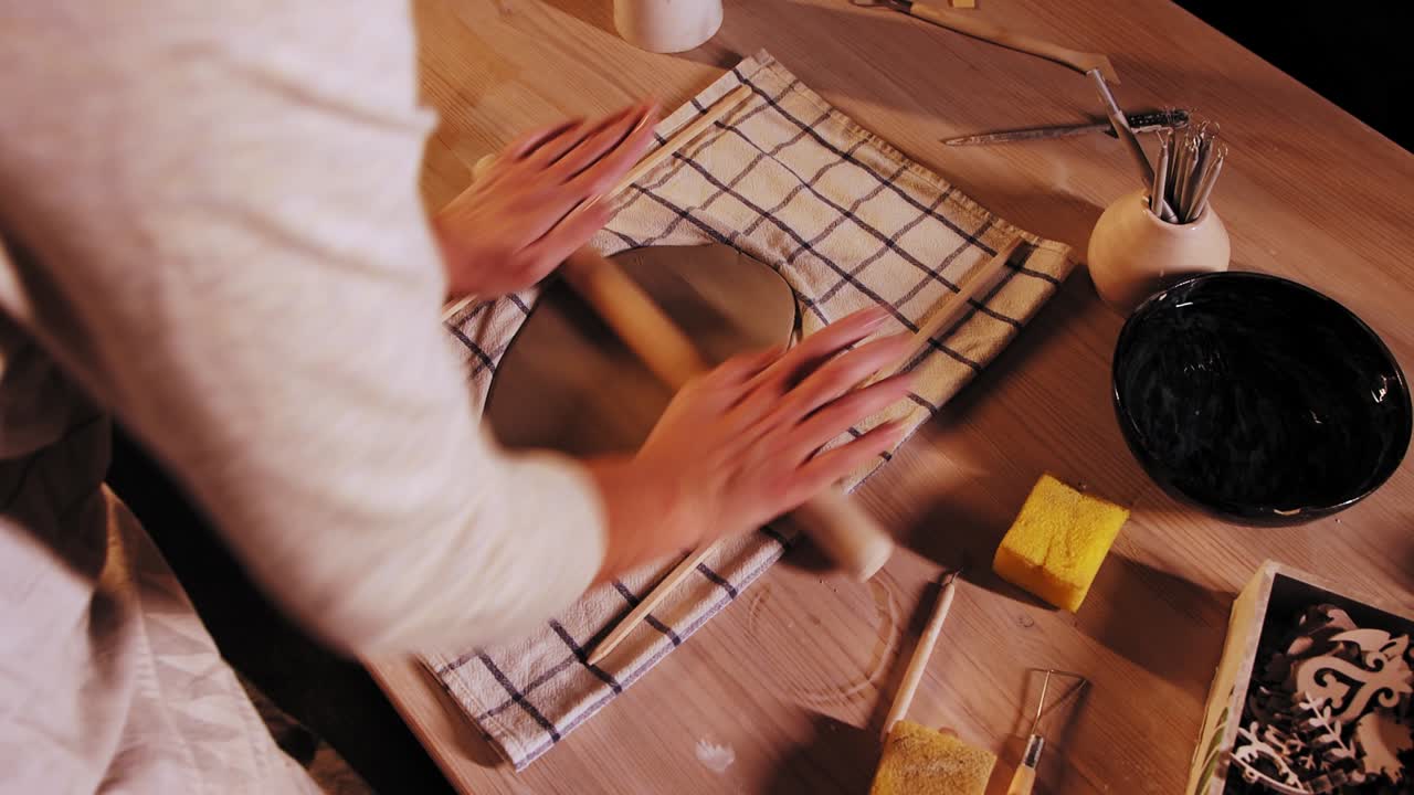 Pottery in the studio - young woman potter flattening clay using a rolling pin