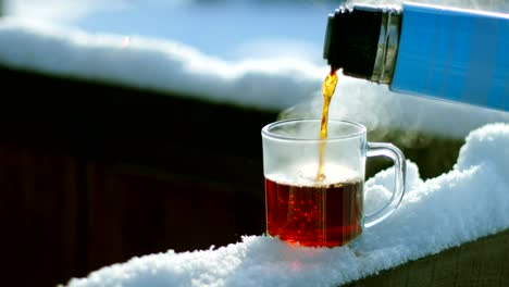 tea pour down to glass standing on snow at tree branch, closeup slow motion shot