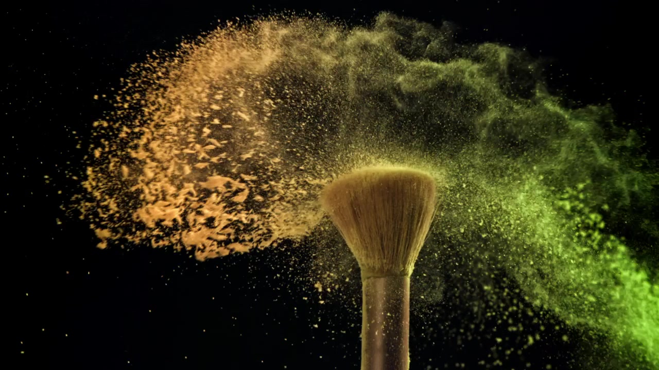 Levende gult og grønt pulver eksploderer fra makeupbørster i slowmotion