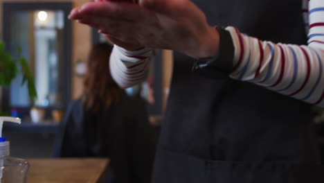 Mid-section-of-female-hairdresser-sanitizing-her-hands-at-hair-salon