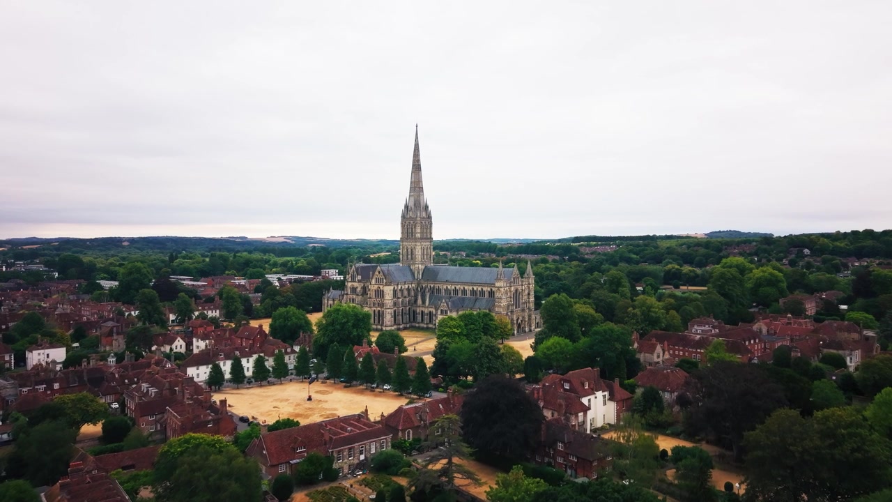 Ampia vista con drone della Cattedrale di Salisbury e della sua imponente guglia medievale, circondata da alberi e tradizionali quartieri residenziali