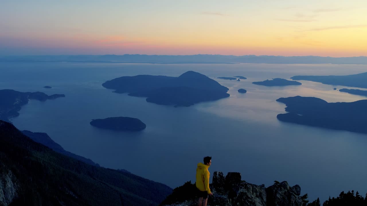 vista aérea de un excursionista en la cima de una montaña al atardecer con vistas al océano en columbia británica, canadá
