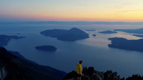 aerail view of hiker on top of a mountain at sunset with ocean views in british columbia canada