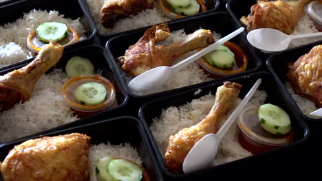 a row of nasi lemak with chicken roasted in lunch boxes container while hands put a plastic spoon with it