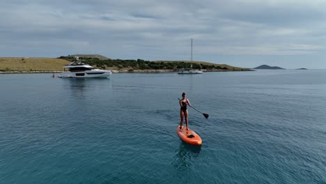 woman standup paddleboarding near the yacht in kornati island, croatia. - aerialshot