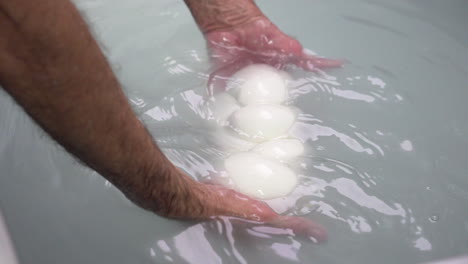 Fabricación-De-Producción-Y-Proceso-De-Elaboración-De-Queso-Mozzarella,-Manos-De-Los-Trabajadores-Que-Manipulan-Suavemente-El-Queso-De-Cuajada-Fresco,-Suave,-Elástico-Y-Crudo,-Amasado-En-Agua-Caliente-Y-Sal