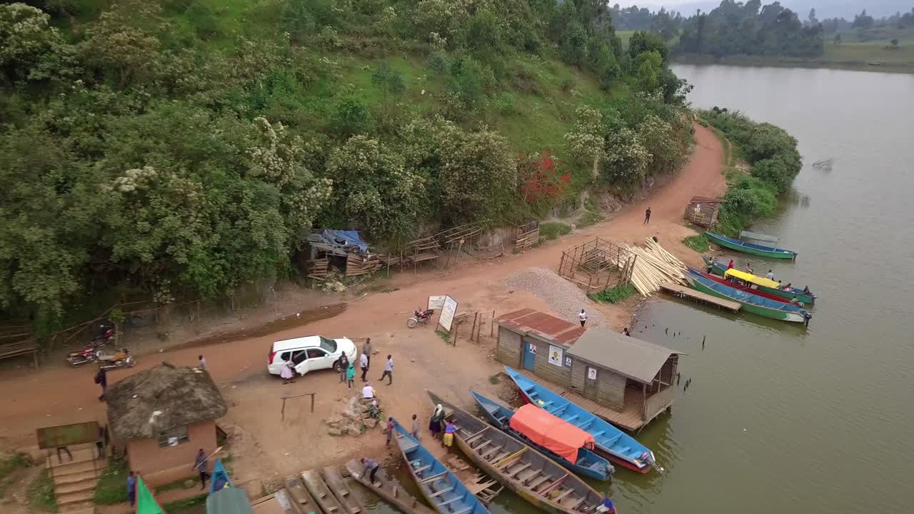 Colorful wooden boats moored on Lake Bunyonyi’s shore near Kabale, Uganda showcases tranquil lakeside scene with vibrant canoes, rustic buildings, and lush green hills in Africa’s second-deepest lake