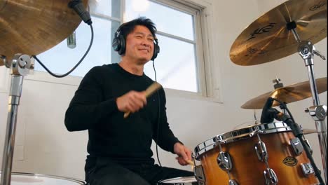 focused asian man playing the drums with headphones in a studio.