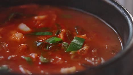 close-up of a bubbling simmering red soup with green onions in a black bowl called kimchi jjgae or kimchi stew, authentic traditional local south korean food