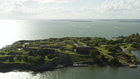 Aerial-view-overlooking-the-walls-and-the-coast-of-the-Susisaari-island,-at-the-Suomenlinna-fortress,-sunny,-summer-day,-in-Helsinki,-Finland---tracking,-tilt-down,-drone-shot