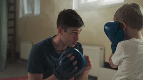 man shows block to kid in martial arts gym. young trainer explains defence and attack techniques to little boy in club slow motion. healthy activity