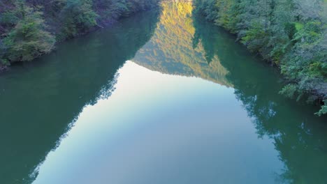 aerial shot of a mountain and forest reflecting on kolpa river surface near kostel, slovenia